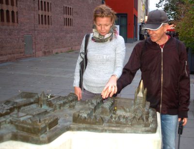 Niewidomy z opiekunką i psem – przewodnikiem dłońmi „ogląda” makietę ratusza.