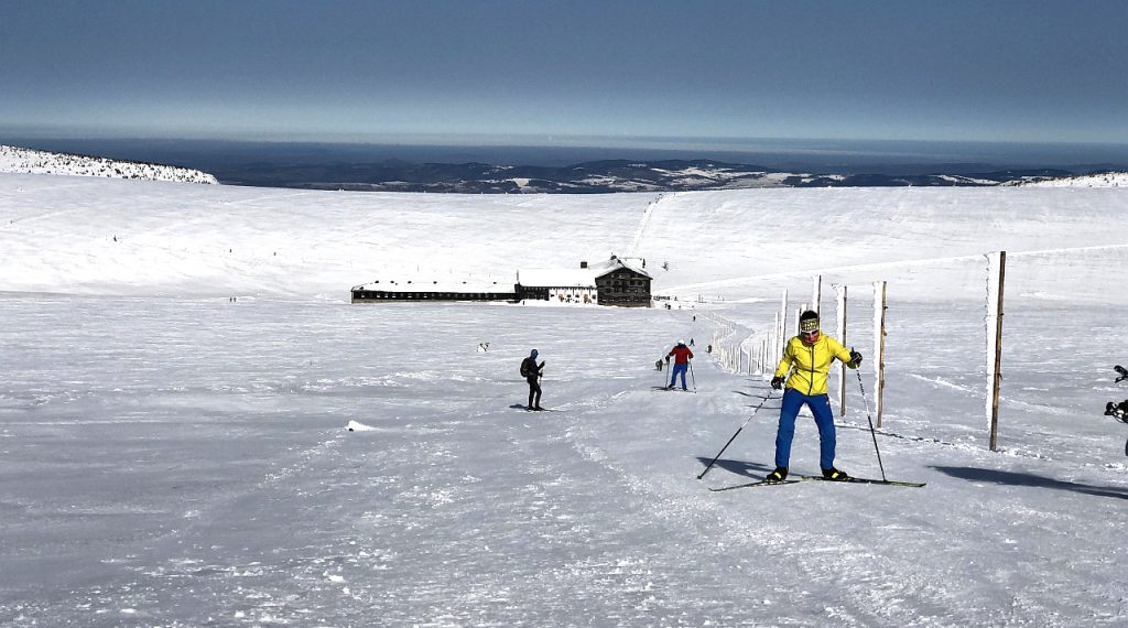 Najstarsze schronisko w czeskich Karkonoszach. Na pierwszym planie narciarze na biegówkach.