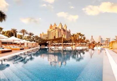 Dubaj. Kąpiel w basenie pod palmami, W tle słynny hotel o kształcie żagla.