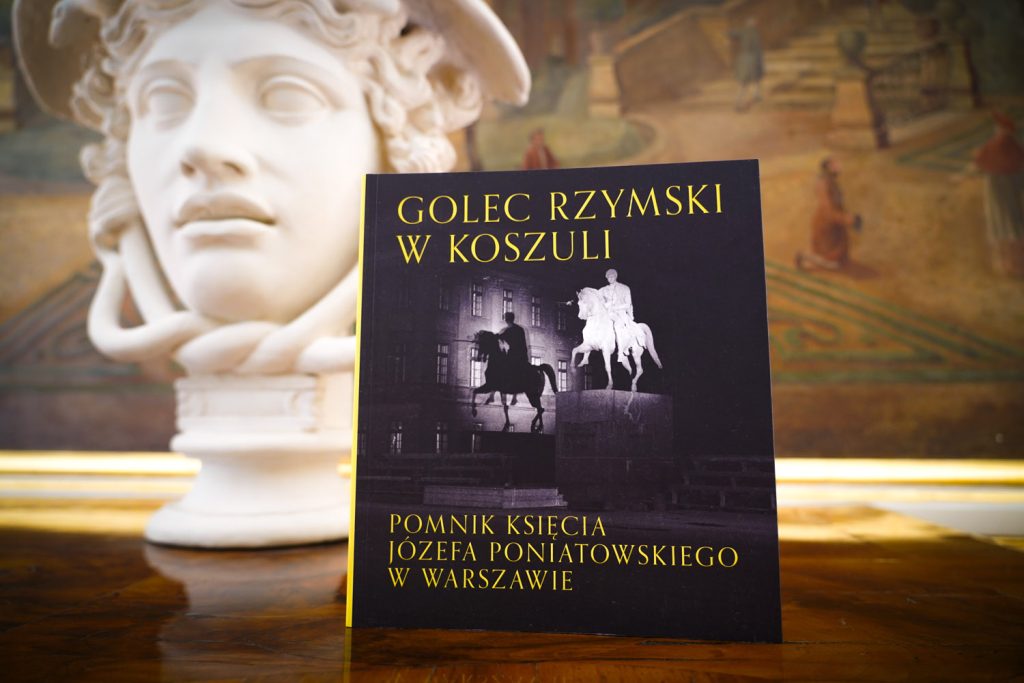 Okładka książki na tle fragmentu ekspozycji muzealnej